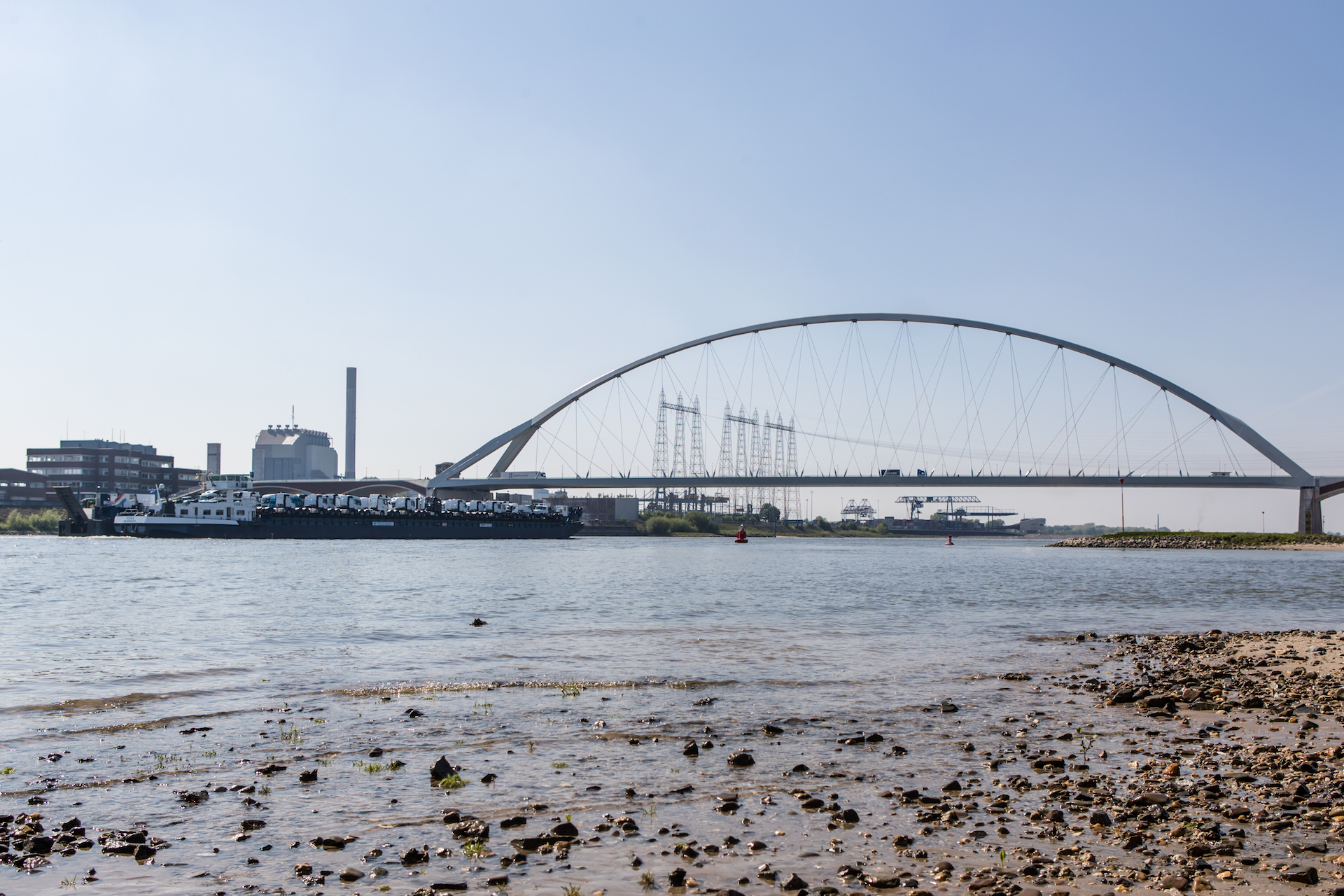 De waalbrug over de Waal bij Nijmegen waar 2 boten onderdoor varen. Onderschrift Lunchlezing Bruggen en logo's van Platform Bruggen en Platform WOW