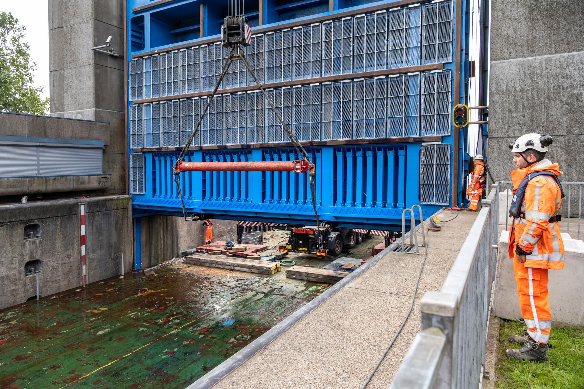 Werkzaamheden bij een sluis. De kranen op het ponton brengen de een sluisdeur in positie onder begeleiding van 2 mannen in beschermende kleding