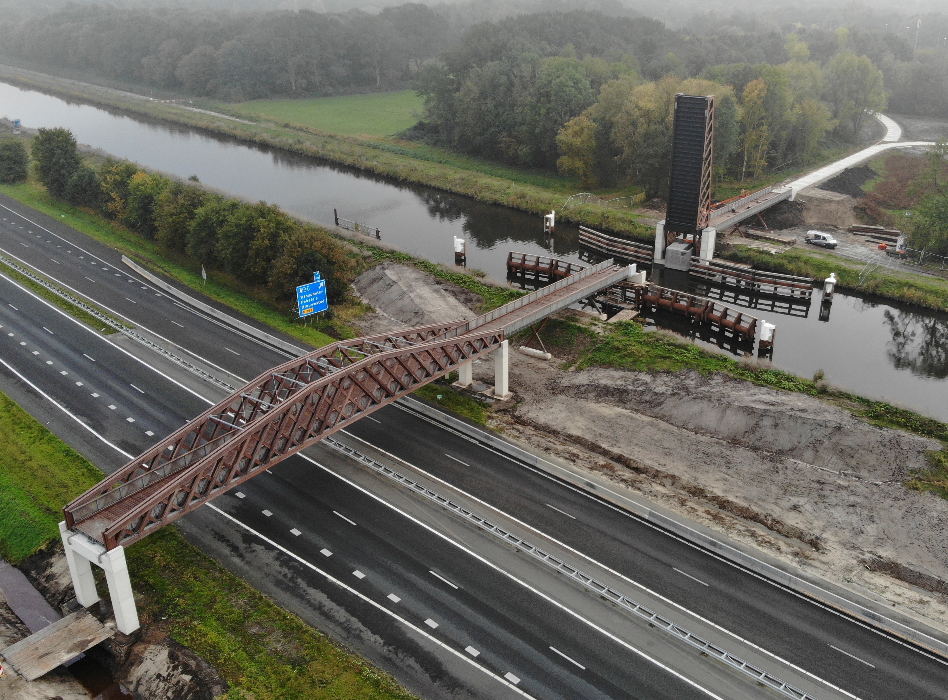 Houten viaduct over een snelweg met paralel daaraan een waterloop met een brug die open stat