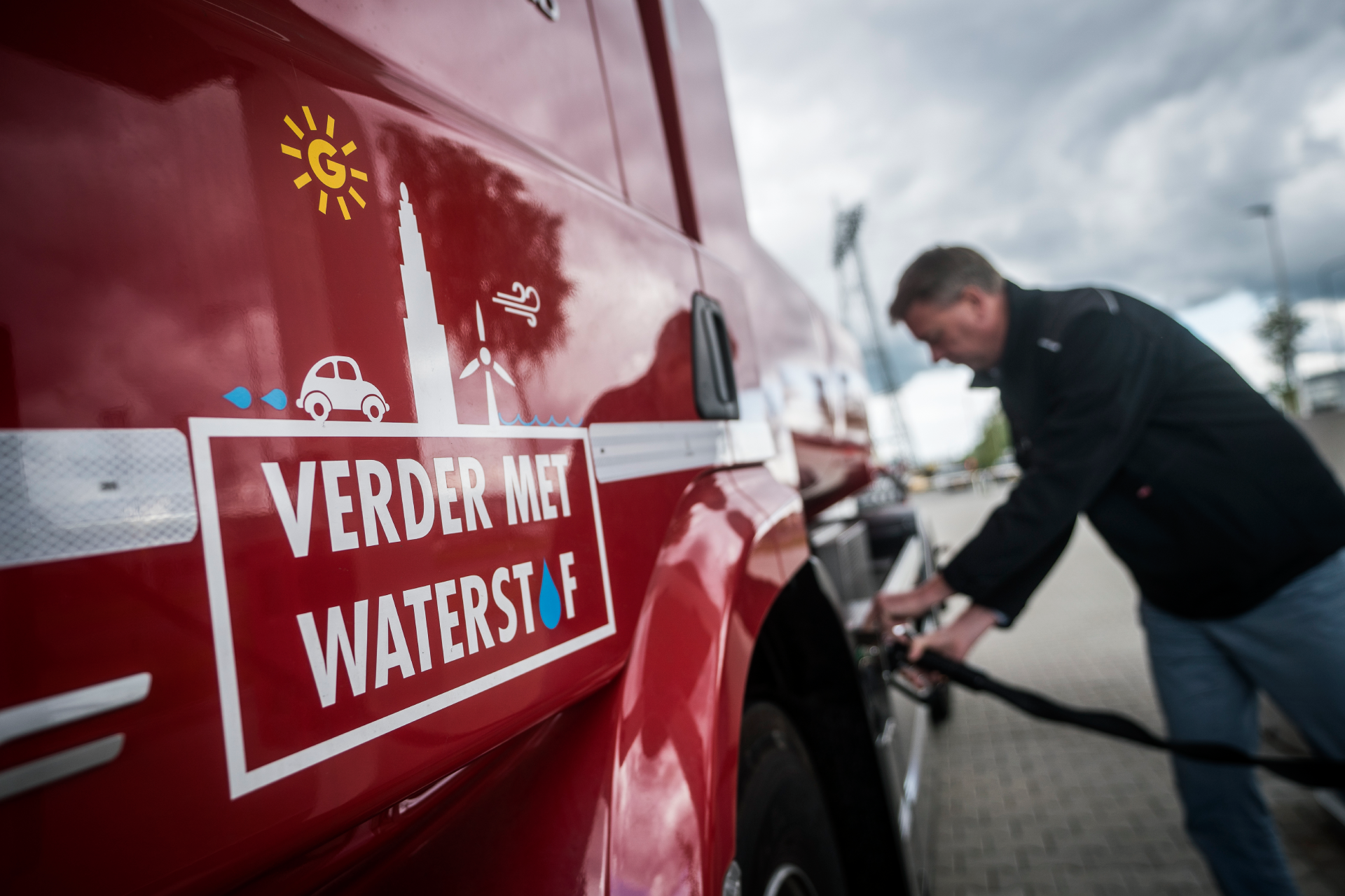 Een rode auto die wordt gevuld met waterstof. Op de auto staat de tekst: verder met waterstof.