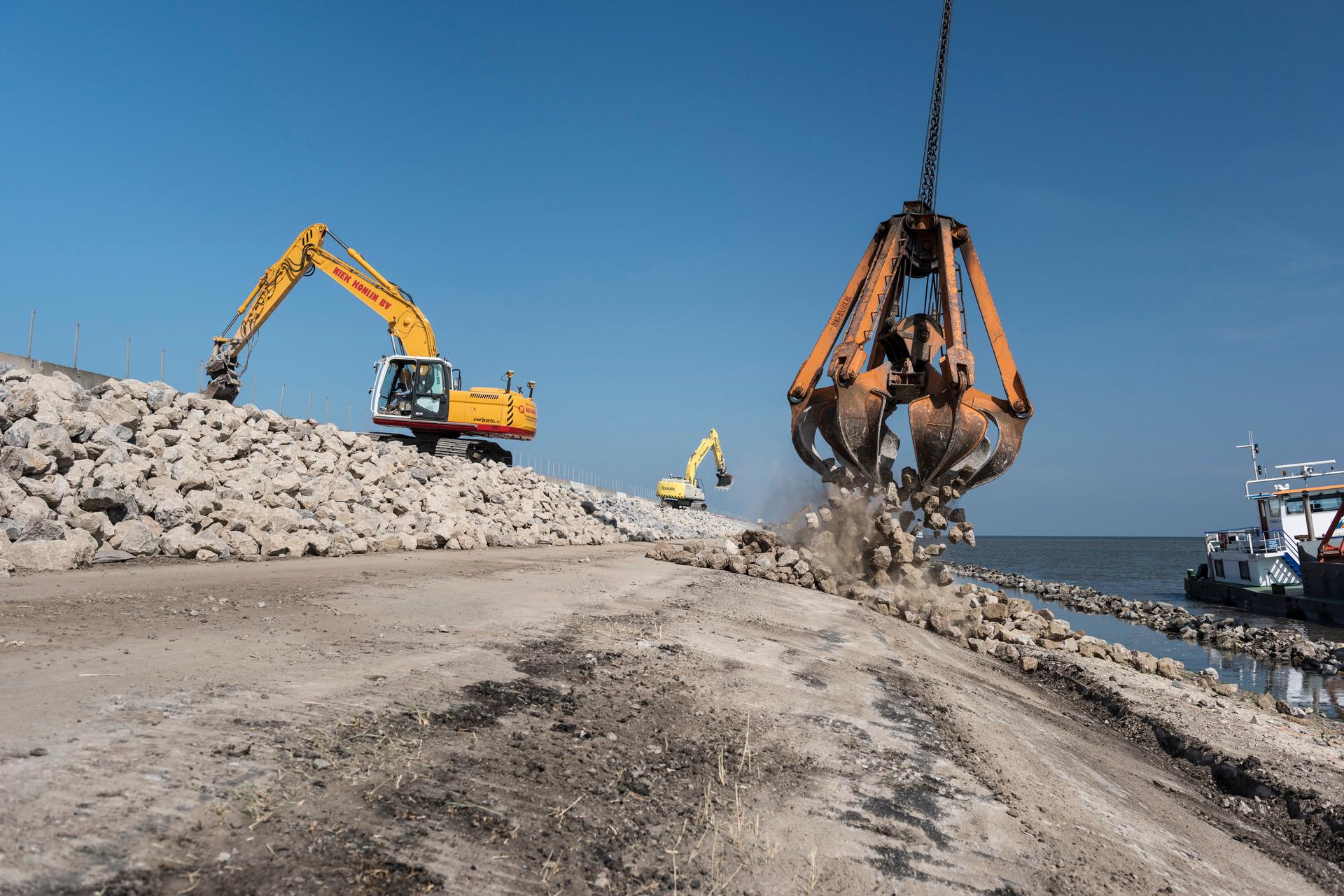 Werkzaamheden ter versterking van de Houtribdijk, een graafmachine stort stenen op de dijk.