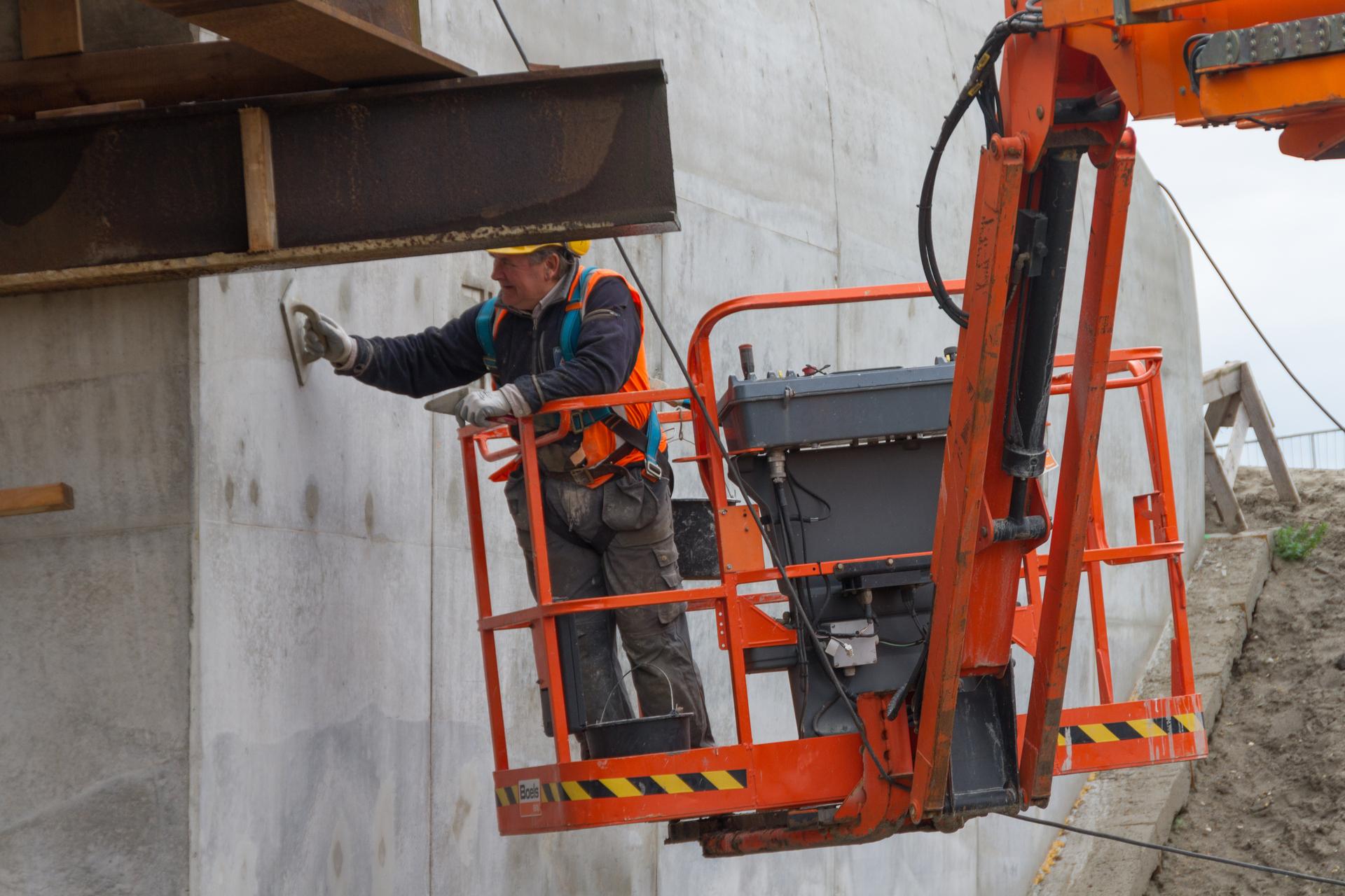 Een wegmedewerker die vanaf een hoogwerker een brug inspecteert bij werkzaamheden omtrent het afwerken, dichten en aansmeren van gaten van het viaduct Zuidkade bij de Verlengde A4