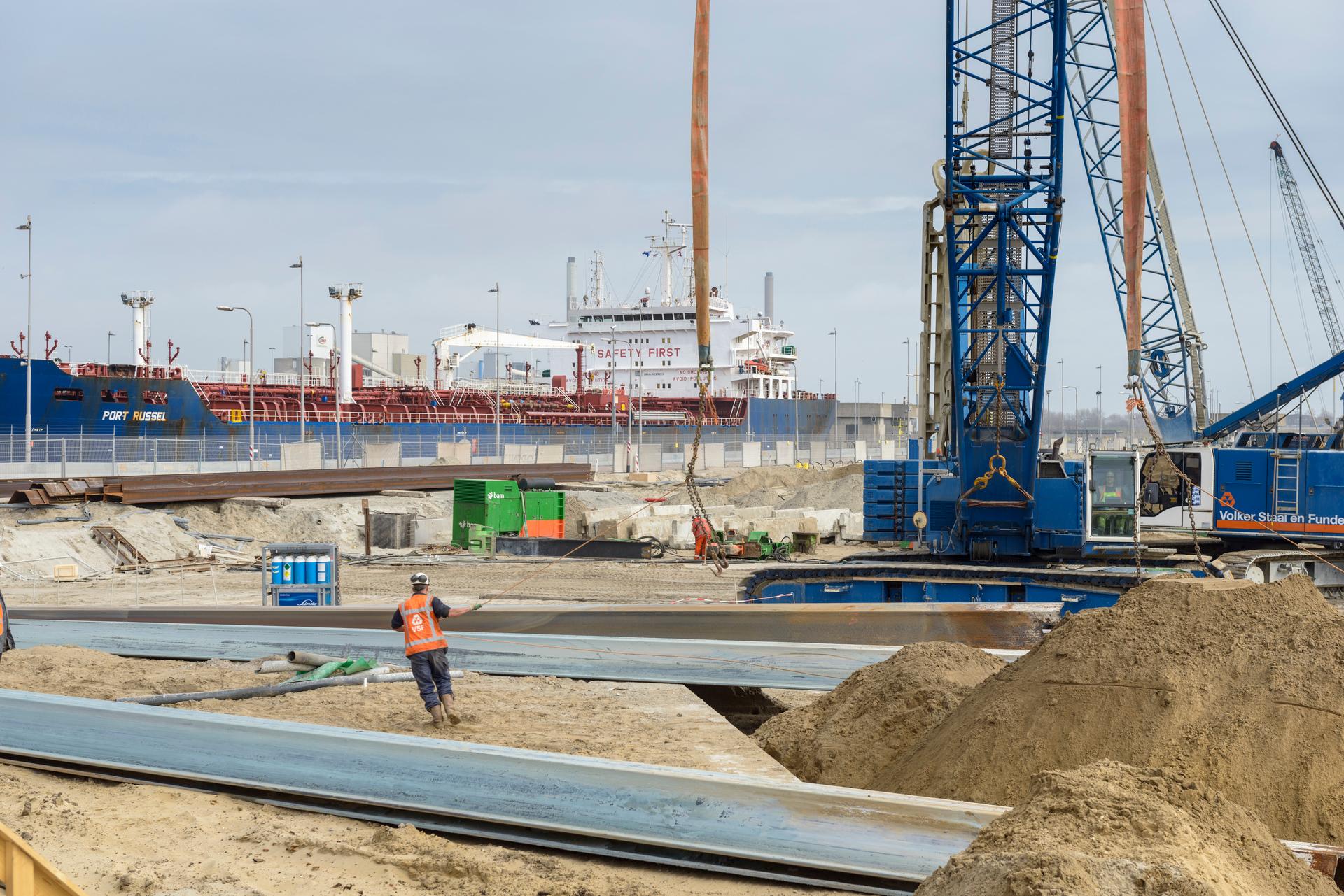 Bouwvakker aan het werk op de bouwplaats met een kraan en schip op de achtergrond.